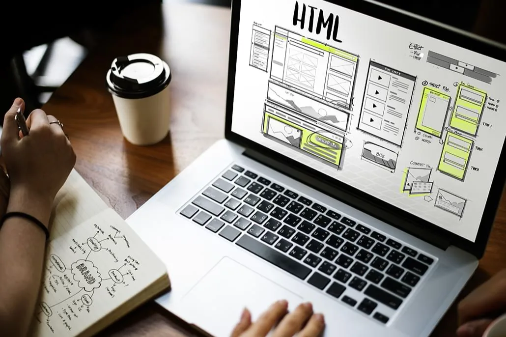 Un ordinateur portable affiche des maquettes de pages web, à côté d’un carnet de croquis.